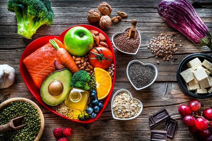 Healthy eating: group of fresh multicolored foods to help lower cholesterol levels and for heart care shot on wooden table. The composition includes oily fish like salmon. Beans like Pinto beans and brown lentils. Vegetables like garlic, avocado, broccoli, eggplant and tomatoes. Fruits like apple, grape, orange and berries. Nuts like almonds and walnuts. Soy products like tofu and soybeans. Cereals and seeds like chia seeds, flax seeds, oatmeal and barley. Olive oil, dark chocolate and yogurt with added sterols and stanols. High resolution 42Mp studio digital capture taken with SONY A7rII and Zeiss Batis 40mm F2.0 CF lens